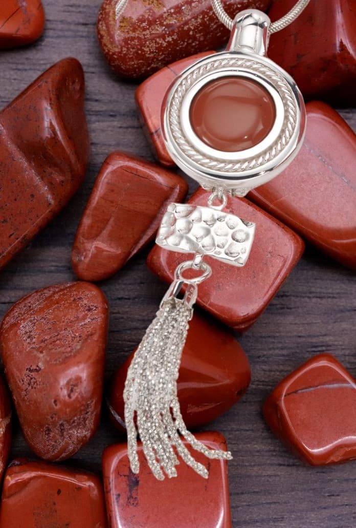 Texture & Tassel necklace with red jasper, resting on tumbled jasper stones